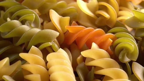 Multicolored italian pasta Fusilli or Rotini rotating in macro background top view side light