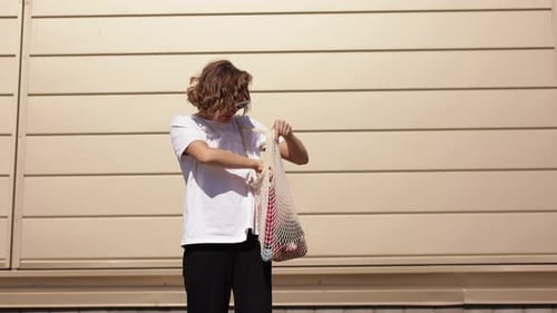 Mujer joven preocupada que busca algo en una bolsa de compras de algodón al aire libre. Accesorio moderno y ecológico