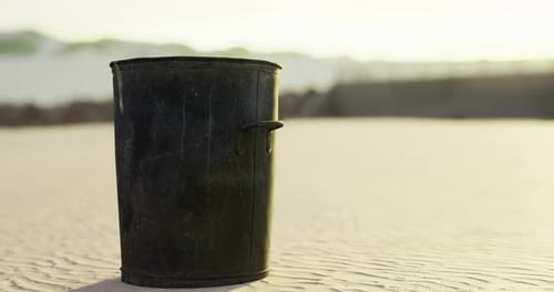 Black Trash Can Standing Alone on a Sandy Beach at Sunset