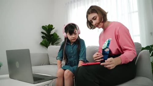 Girl watches woman play toy guitar on sofa