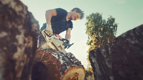 Man Cuts Tree Trunk with Chainsaw Outdoors