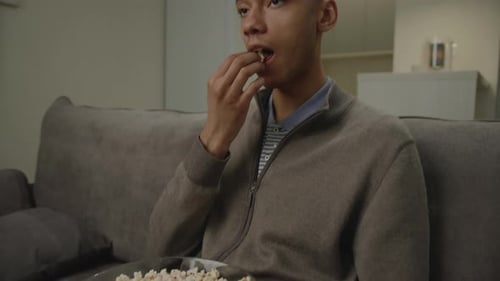 Young Adult Eats Popcorn at Home on Couch