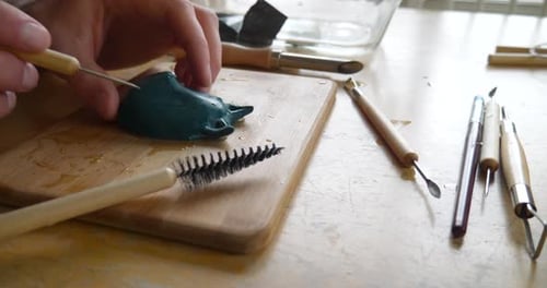 Close up on an artists hands carving and marking with a sharp clay sculpting tool on a mask figurine