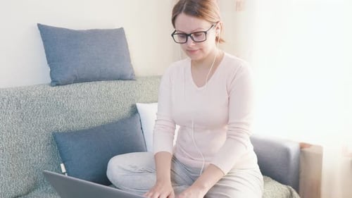 Junge Freelancerin arbeitet zu Hause am Laptop und sitzt auf der Couch