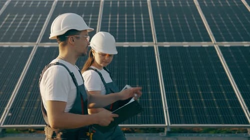 Workers in Overalls Walk Around the Solar Panel Area and Analyze Data