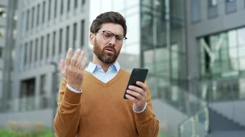 Shocked worried businessman reading bad news on mobile phone while standing on the street near