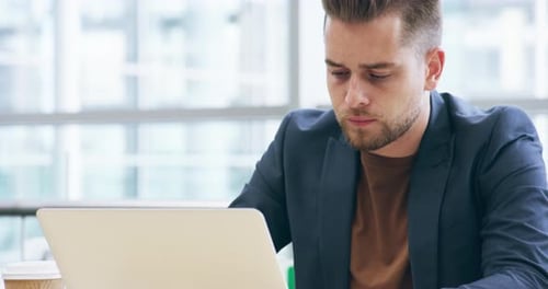 Imágenes de vídeo en 4K de un apuesto joven empresario trabajando en su portátil en la oficina
