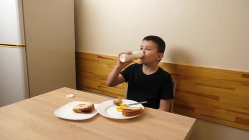 Child Drinks Milk and Eats Breakfast at Table