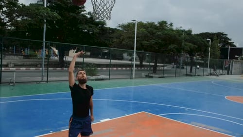 young man with a beard plays basketball alone