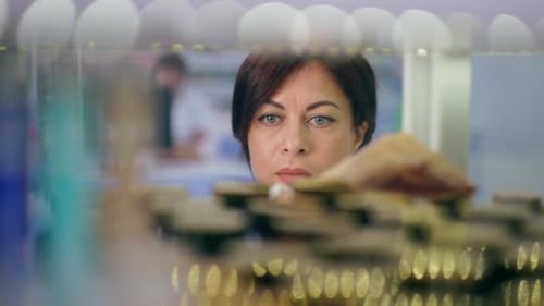 View Behind Shelf of Concentrated Female Pharmacist Examining Medications in Drugstore