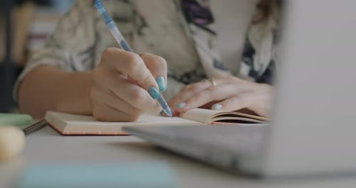 Woman Writes in Notebook Near Laptop