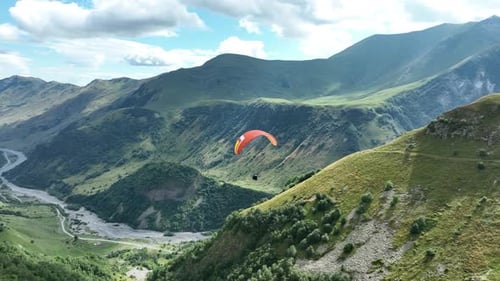 Aerial view of a deep mountain gorge with a winding riverbed, lush green slopes, and rugged peaks