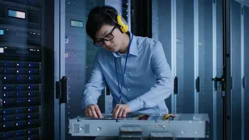 In the Modern Data Center: IT Engineer Wearing Protective Muffs Installs New Hardware for Server Ra