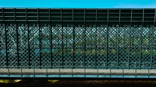 Railway Bridge Featuring Dense Lattice Metal Walls and Pedestrian Walkway Below Steel Structure