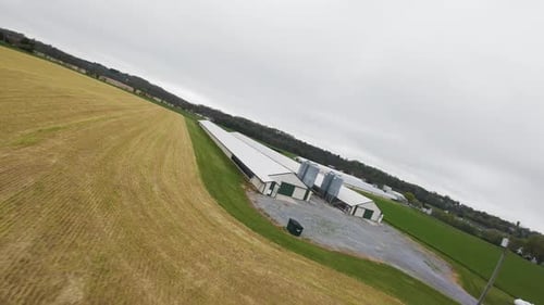 Fpv drone flight over farm field with barn for animals during grey sky in countryside of american to