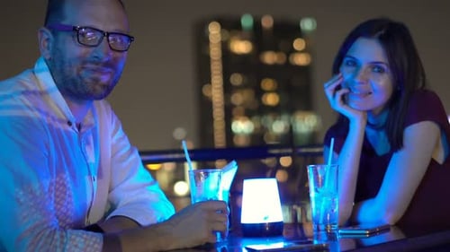 Happy couple enjoying cocktails together on a rooftop terrace at night