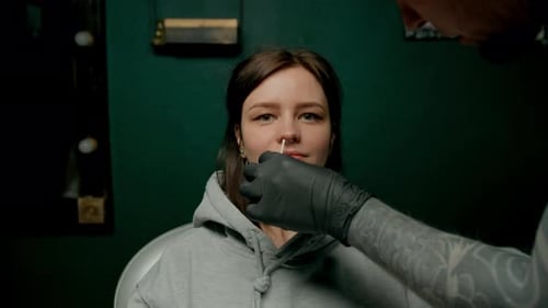 Interior de un estudio de piercings: el maestro de piercings hace un piercing para una niña, piercing para el tabique nasal