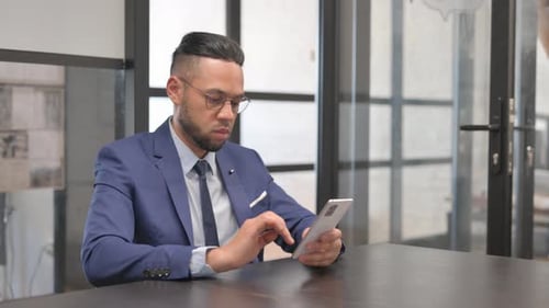 Hispanic Businessman Typing Message on Phone at Workspace