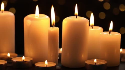 Burning candles against black background with blurred lights, closeup. Camera moving right