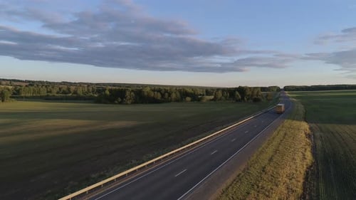 Aerial View of Trucks Driving on an Intercity Road Between Green Fields in the Beautiful Morning of