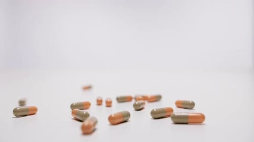 Medicine capsules falling on white background in slow motion.