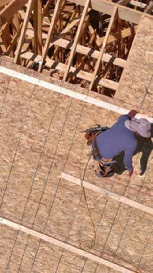 Building Workers Hammer Nails Into Plywood on Roof of a Future Home