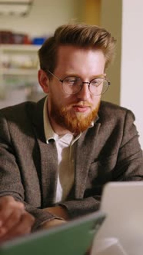 Focused Young Man with Glasses Working Intently on Laptop in Cozy Indoor Workspace Transitioning