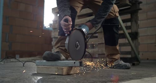 Worker grinding metal with handheld electric grinder, sparks scattering across floor, intense