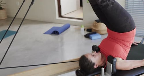 Fit senior caucasian woman stretching on reformer in pilates studio, unaltered, in slow motion