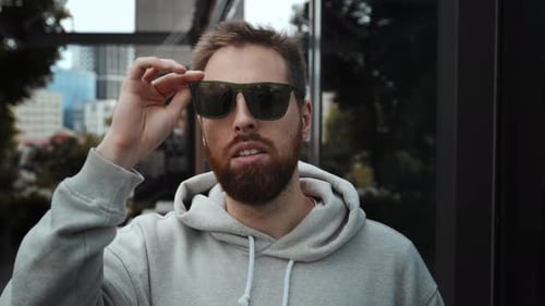 Bearded Man Puts on Stylish Sunglasses in City