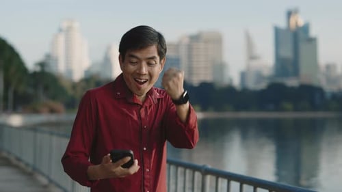 Excited Man Celebrates with Smartphone in City Park