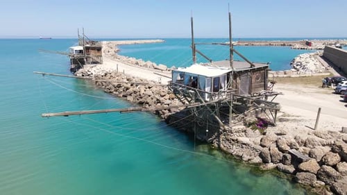Wide angle orbiting drone shot of an old wooden structure called a "Trabucco" that is an ancient met