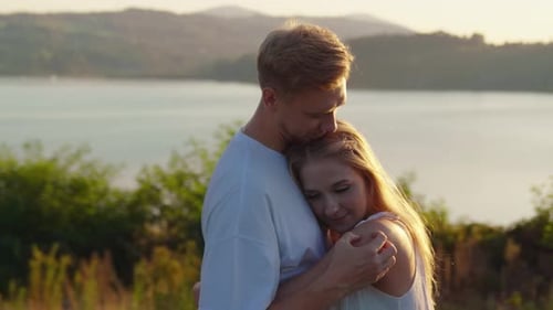 Young Couple Hugging while Standing by the Lake at Sunset