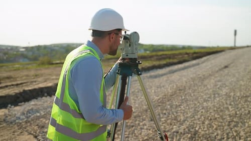 Surveyor Engineer Using Theodolite for Topographic Measurement on Road Construction Site