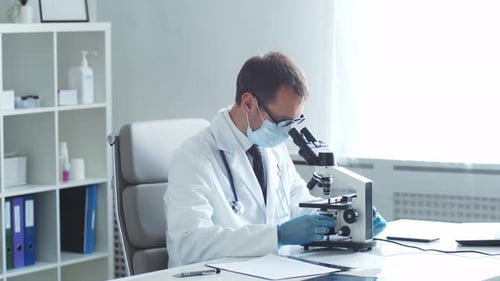 Professional Medical Doctor Working in Hospital Office Using Microscope