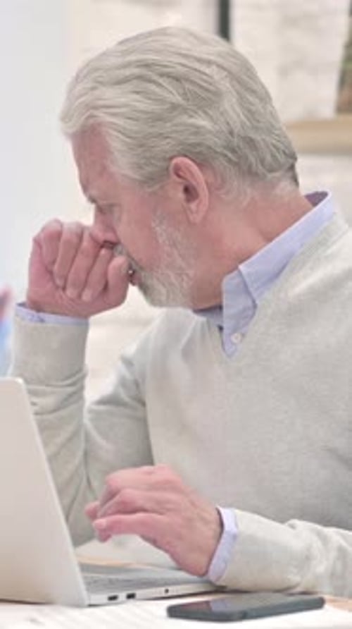 Senior Man Working at Computer Coughing into Fist