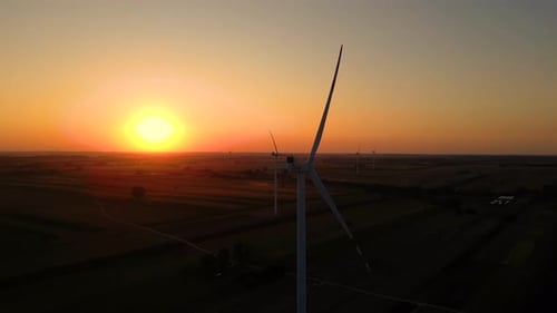 Watch as the sun sets over a serene landscape of wind turbines in a vast field, showcasing the beaut