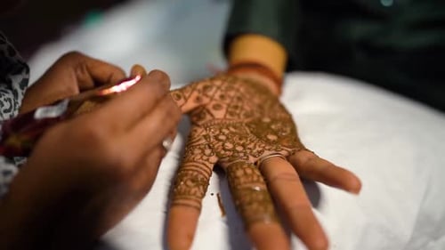 A mehndi artist applying detailed henna designs on the groom’s hand during a traditional Indian