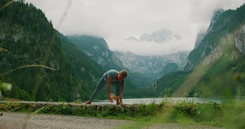 Woman stretches beside a serene lake, embraced by towering mountains and mist, embodying tranquility