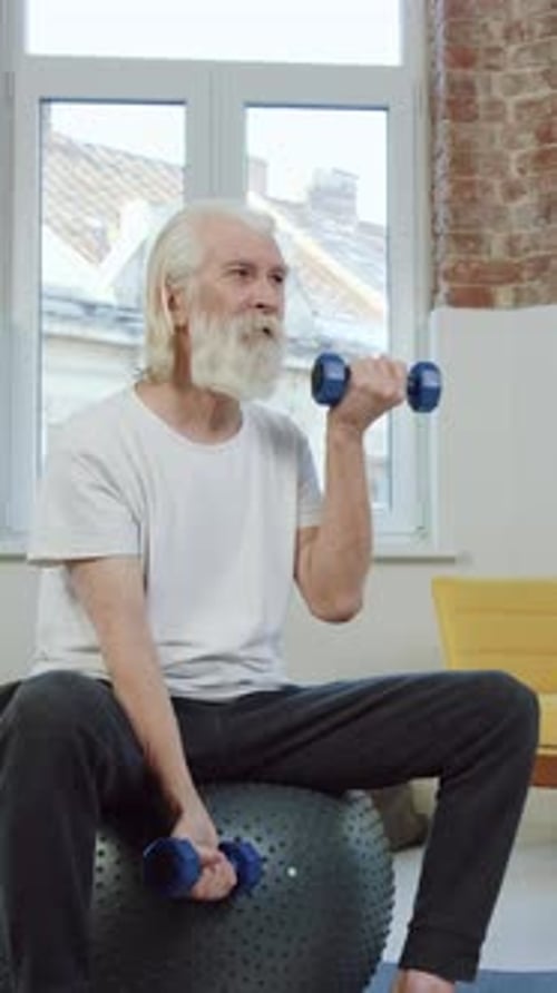 Senior Man Lifting Dumbbells While Sitting on Exercise Ball