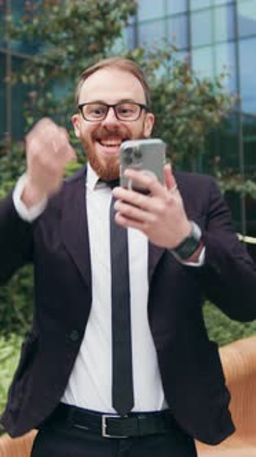 Excited Businessman Celebrates Success with Phone Outside Building