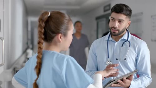 Diverse male and female doctors discussing work using tablet in hospital corridor, slow motion