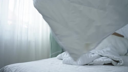 Young Woman Making Bed in Bright Bedroom