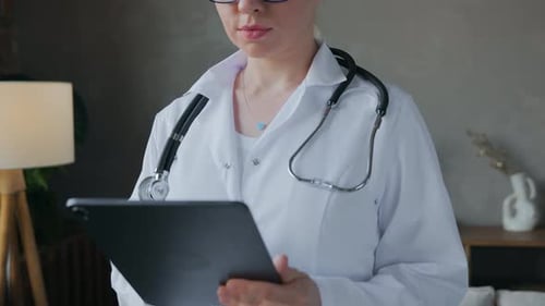 The Doctor is Standing in the Office and Uses an Electronic Tablet
