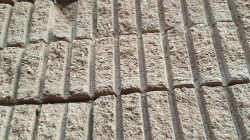 Slide panning slow motion footage of a sandstone brick building wall, rough texture pattern with con