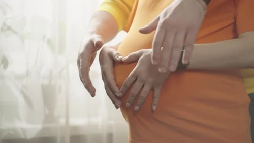 Une femme qui attend un enfant fait un cœur sur son ventre avec ses mains