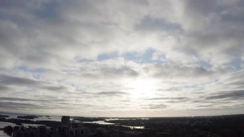 Tilt down arial view of coastal city and sunset behind the clouds.