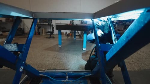 Trabajador calificado en equipos de protección que suelda un marco de metal con chispas brillantes en una industria