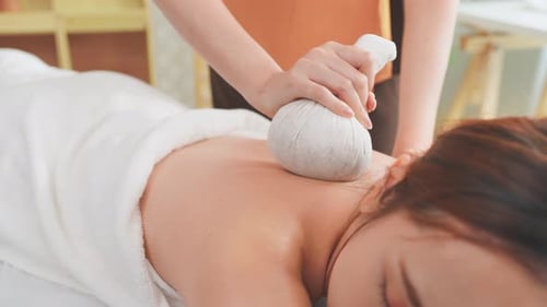 Asian young woman getting thai hot compress massage with herbal bags.