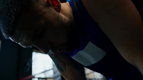 Tired boxer after hard training in the gym wearing sportswear and black boxing gloves